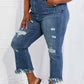 Woman wearing Undone Chic Straight Leg Risen Jeans with distressing, raw hems, and waist details paired with a white crop top and green sandals.