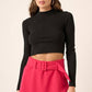 Model wearing a black mock neck long sleeve crop knit top paired with a pink belted mini skirt, showcasing a chic outfit.