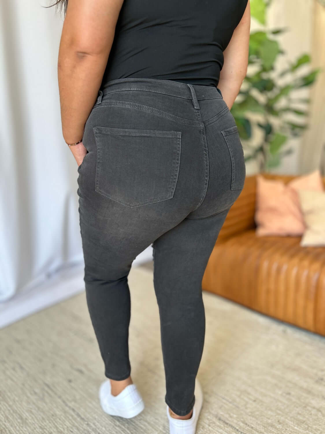 Woman wearing RFM Full Size High Rise Tummy Control Skinny Jeans showcasing back pockets and slimming fit in a cozy setting.