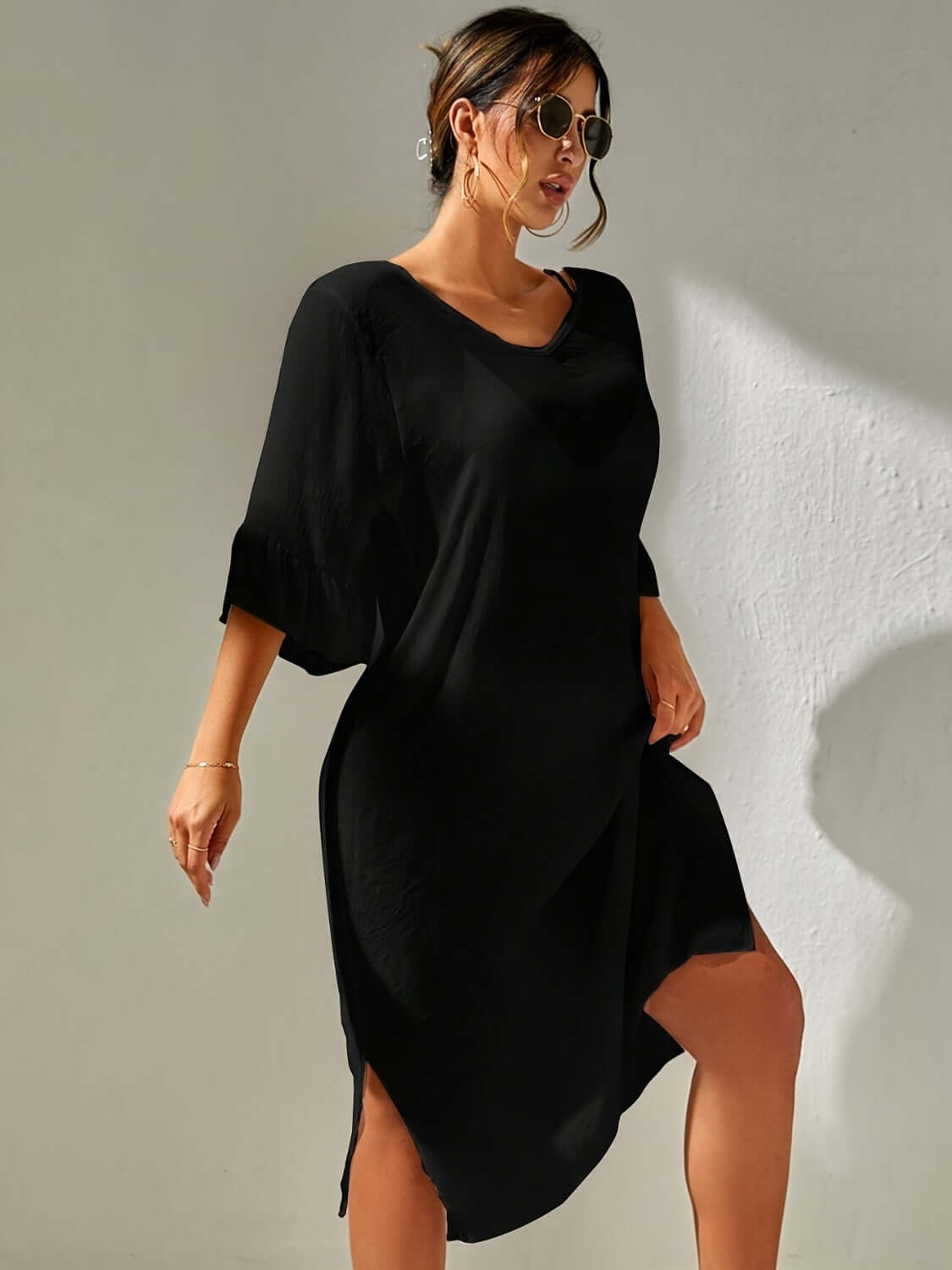 Woman wearing a black slit V-neck flounce sleeve cover-up. Backless and sheer with no stretch, made of 100% polyester.