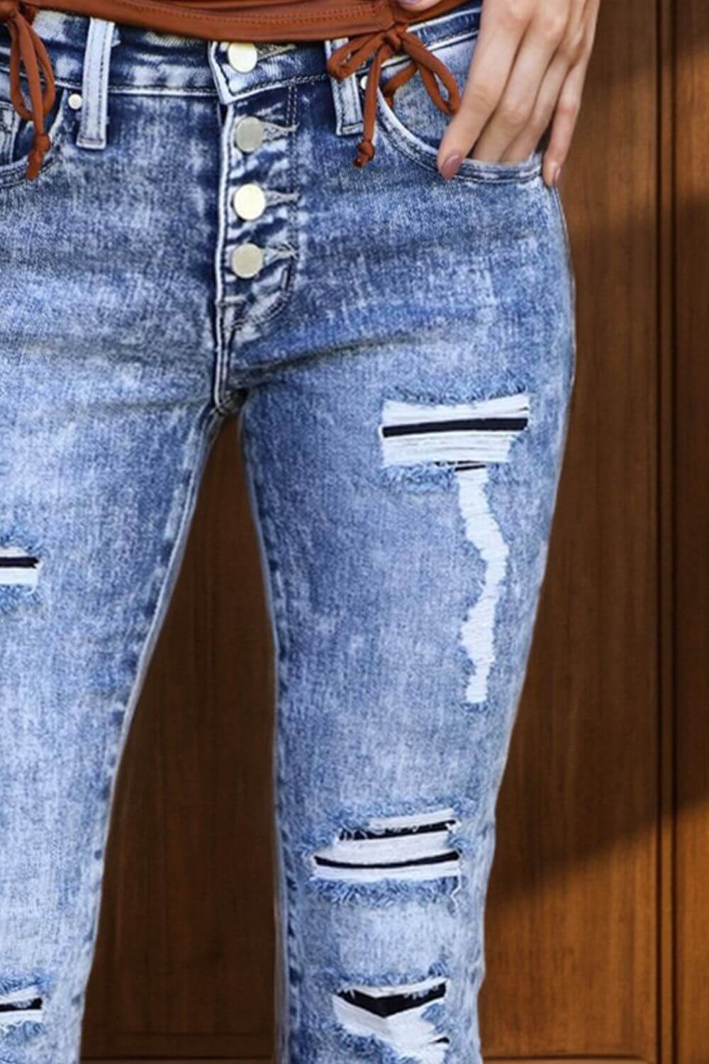 Close-up of distressed button-fly bootcut jeans with pockets, featuring a trendy petite fit and stylish rips.