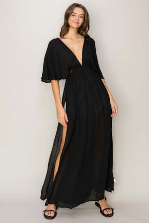 Woman wearing a black tie back maxi split cover up dress with a plunging neck, batwing sleeves, and long side slits.