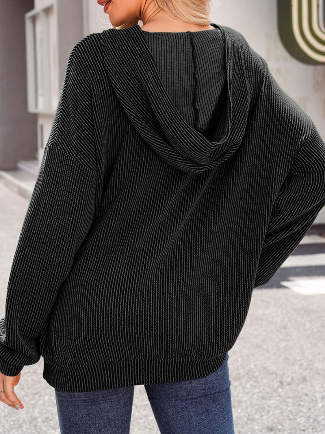 Woman wearing textured kangaroo pocket long sleeve hoodie in black, back view showing hood detail.