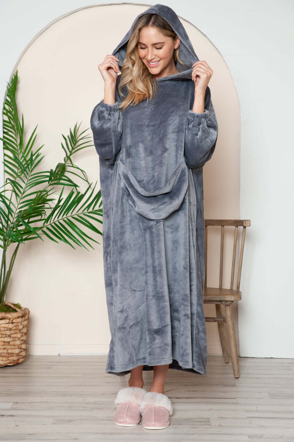 Cozy woman in a hooded grey midi lounge dress with pockets, perfect for fall lounging, paired with fluffy slippers.