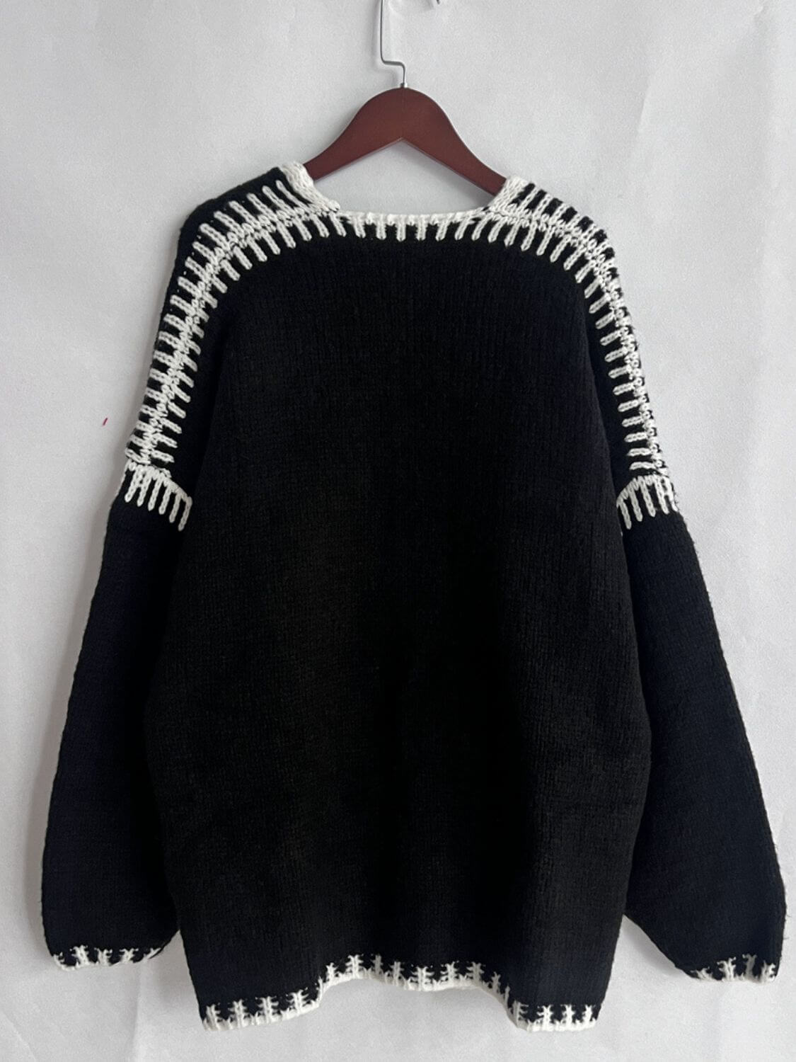 Stylish black cardigan with contrast stitching on a hanger, showcasing trendy open front and dropped shoulder design.