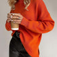 Woman wearing an orange turtleneck dropped shoulder sweater with side slits, holding a coffee cup, and dressed in leather pants.