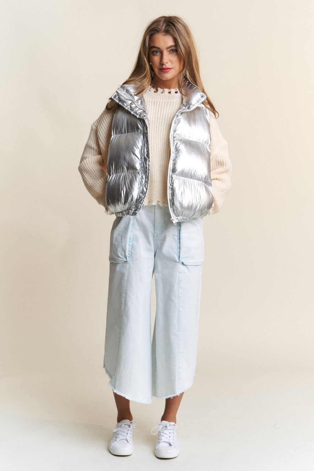 Trendy metallic puffer vest with snap and zipper closures styled over a cozy sweater and denim, showcasing chic layering fashion.