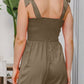 Woman wearing olive green bodice smocked sleeveless jumpsuit with tie straps, back view, standing outdoors.