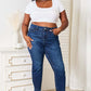 Woman modeling Judy Blue High Waist Released Hem Slit Jeans in deep indigo wash, paired with a white crop top for a chic look.