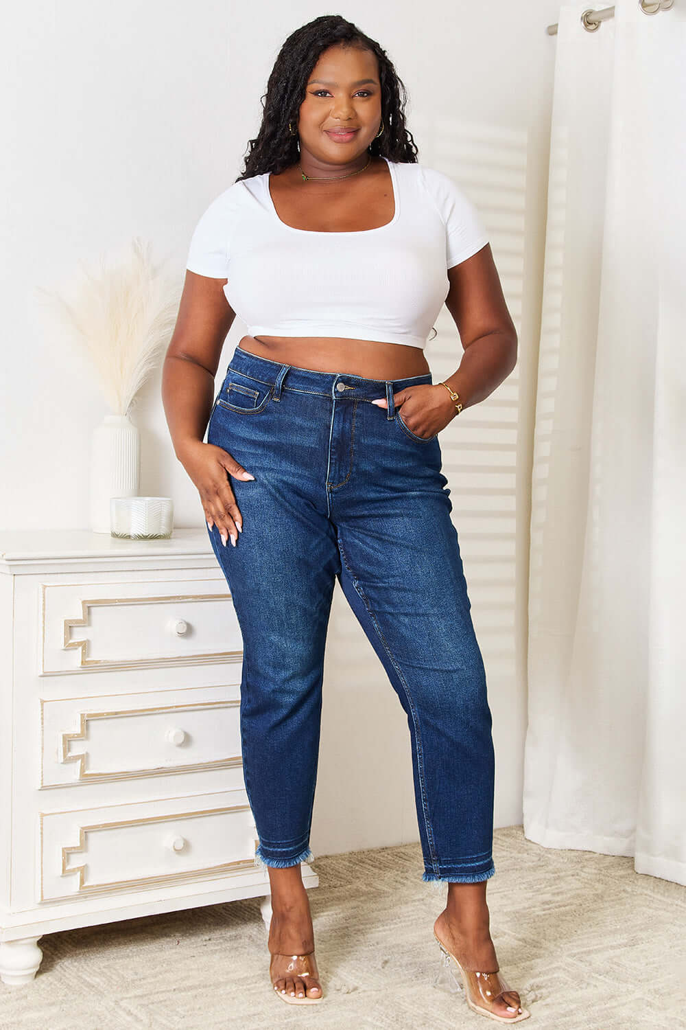 Woman modeling Judy Blue High Waist Released Hem Slit Jeans in deep indigo wash, paired with a white crop top for a chic look.