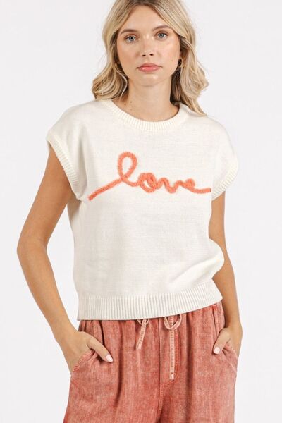 Stylish woman in cream cap sleeve knit top with 'love' lettering, paired with casual peach pants.