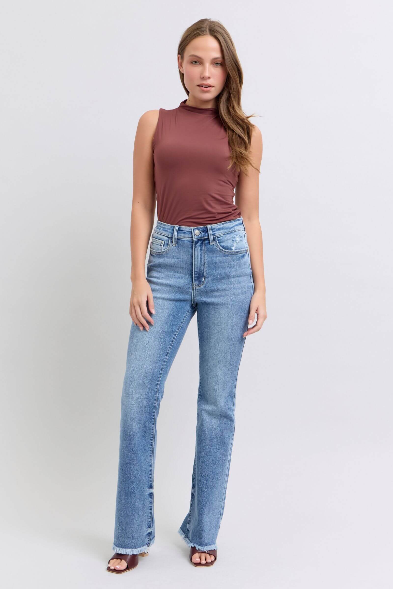 Stylish woman wearing Judy Blue high rise bootcut jeans with a raw hem and a trendy brown sleeveless top.