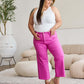 Woman wearing pink high waist tummy control raw hem jeans by RFM Jeans, styled with a white tank top and beige wedges.