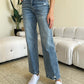 Woman wearing Judy Blue High Waist Distressed Straight Jeans with white shoes in a casual living room setting