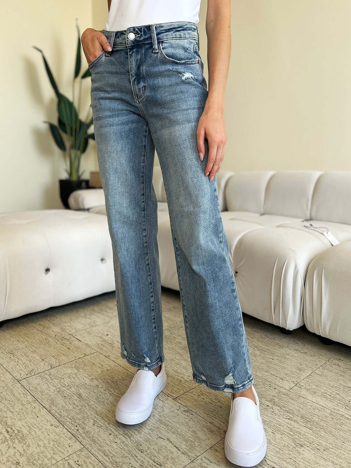 Woman wearing Judy Blue High Waist Distressed Straight Jeans with white shoes in a casual living room setting