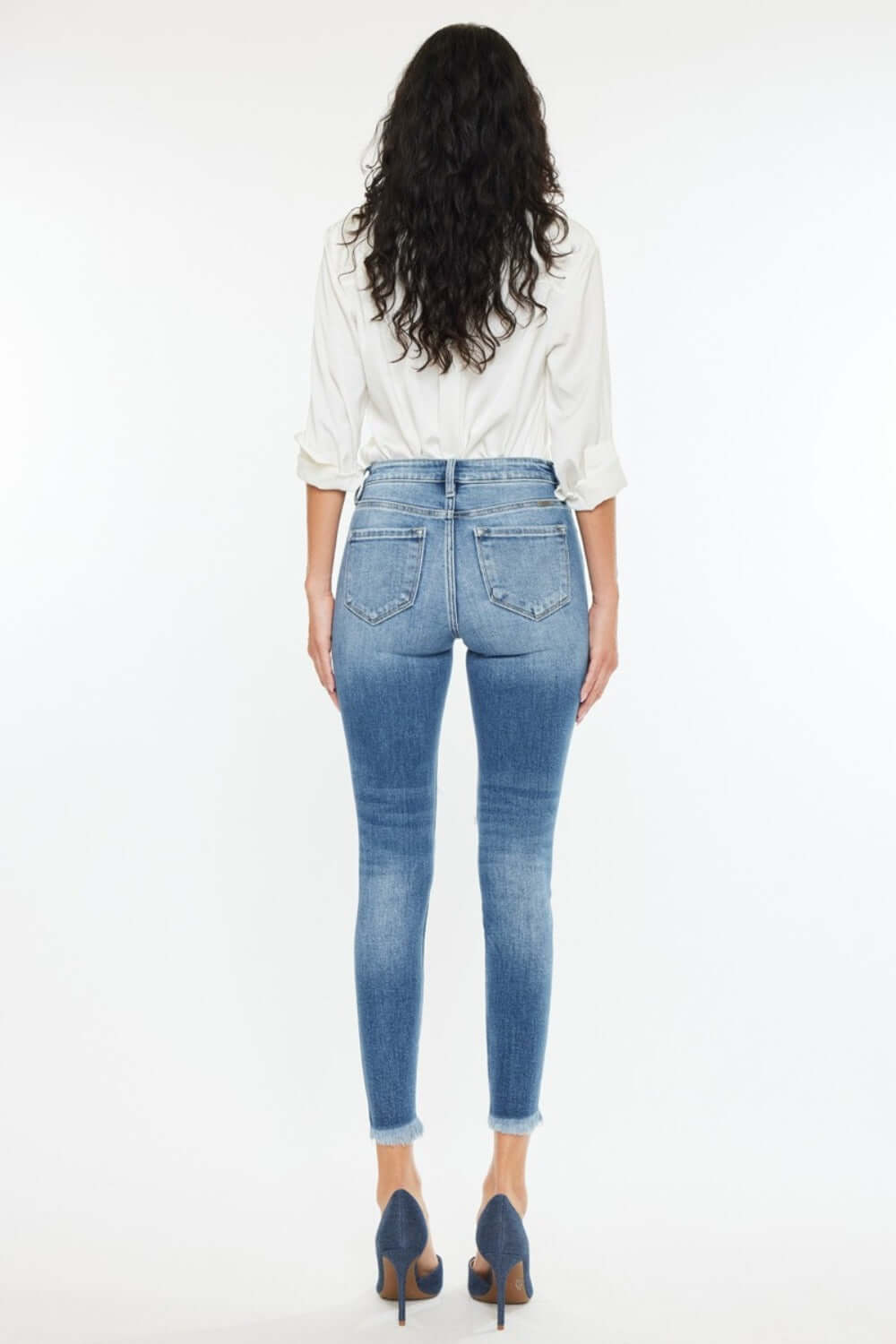 Woman wearing high rise frayed ankle skinny jeans in medium wash with a white top, showcasing back view of the denim’s fit and style