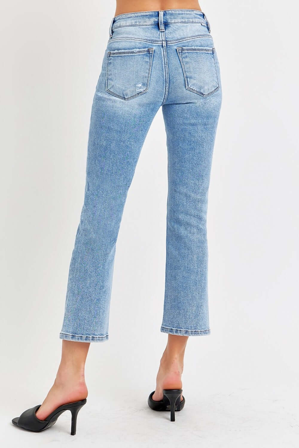 Woman wearing low rise crop slim straight jeans with raw hem and pocketed design, paired with black heels.