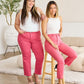 Two women in matching pink RFM Jeans sitting and standing in a stylish room, showing the versatility and comfort of the jeans.