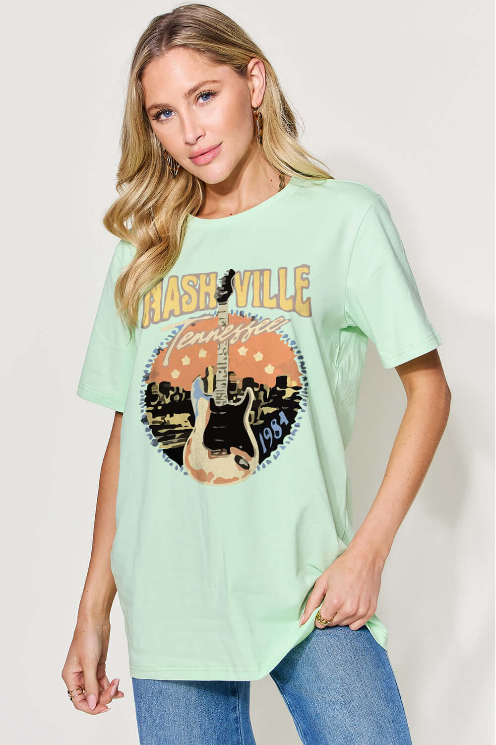 Woman wearing a graphic round neck short sleeve t-shirt with "Nashville" print, slightly stretchy cotton-spandex blend, paired with blue jeans.