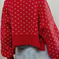 Woman wearing red sweater with small white heart pattern, showcasing cozy fall fashion paired with light blue jeans.