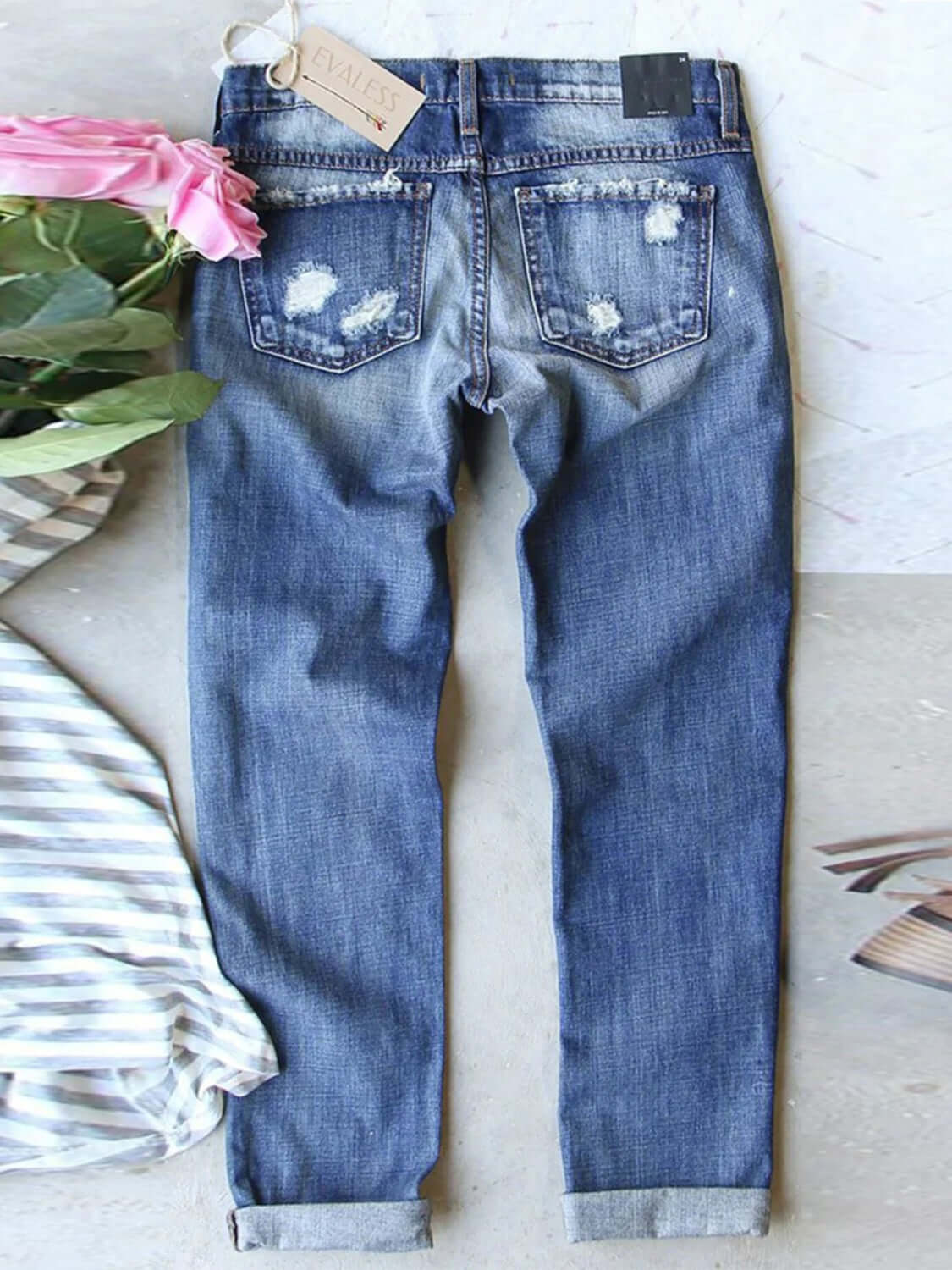 Distressed printed straight jeans in blue color with back view, surrounded by flowers and stripped cloth, perfect for adding unique touch to denim collection