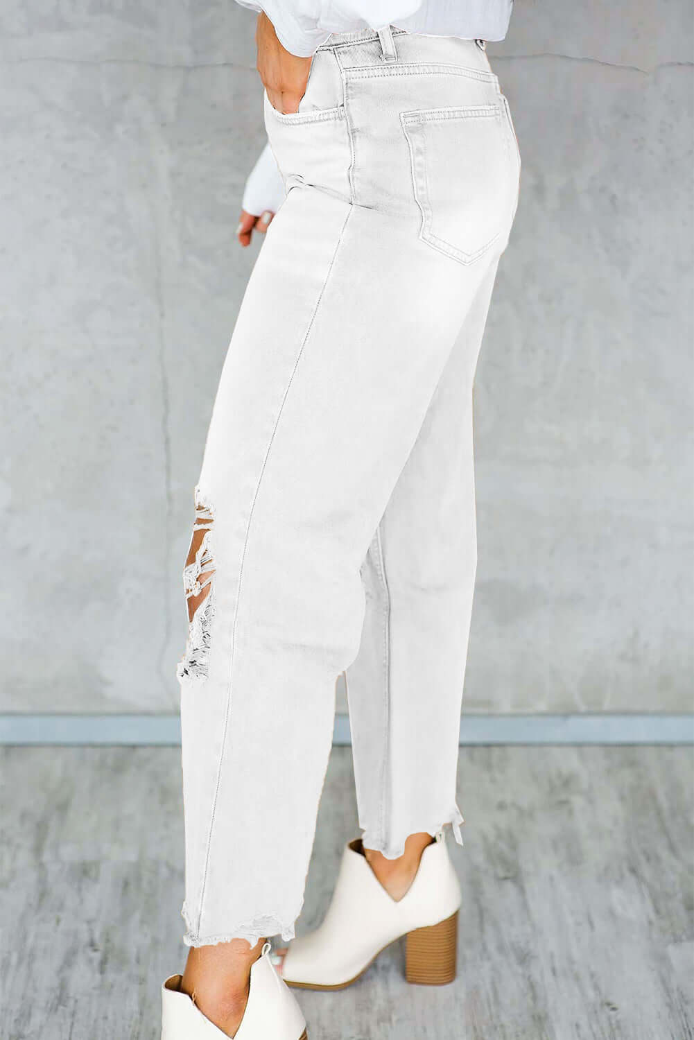 Side view of Distressed Raw Hem Jeans with Pockets, featuring trendy design and white boots against a gray background.