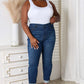 Woman wearing skinny cropped Judy Blue Jeans styled with a white tank top and heels in a modern bedroom.