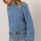 Stylish woman in blue cable-knit mock neck sweater paired with denim skirt, showcasing cozy autumn fashion.