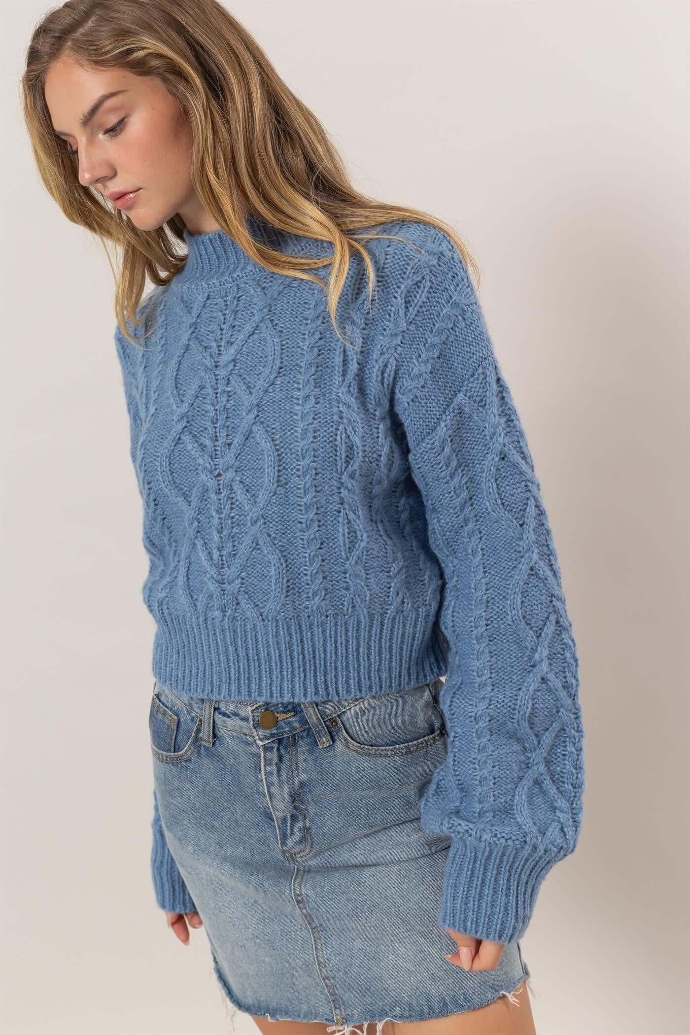 Stylish woman in blue cable-knit mock neck sweater paired with denim skirt, showcasing cozy autumn fashion.