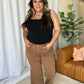 Woman wearing RFM High Rise Garment Dye Wide Leg Jeans in rich brown, standing in a stylish room with a chic and relaxed vibe.