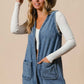 Stylish woman wearing a BiBi braided trim open front denim vest with pockets, paired with a fun hat and long-sleeve top.