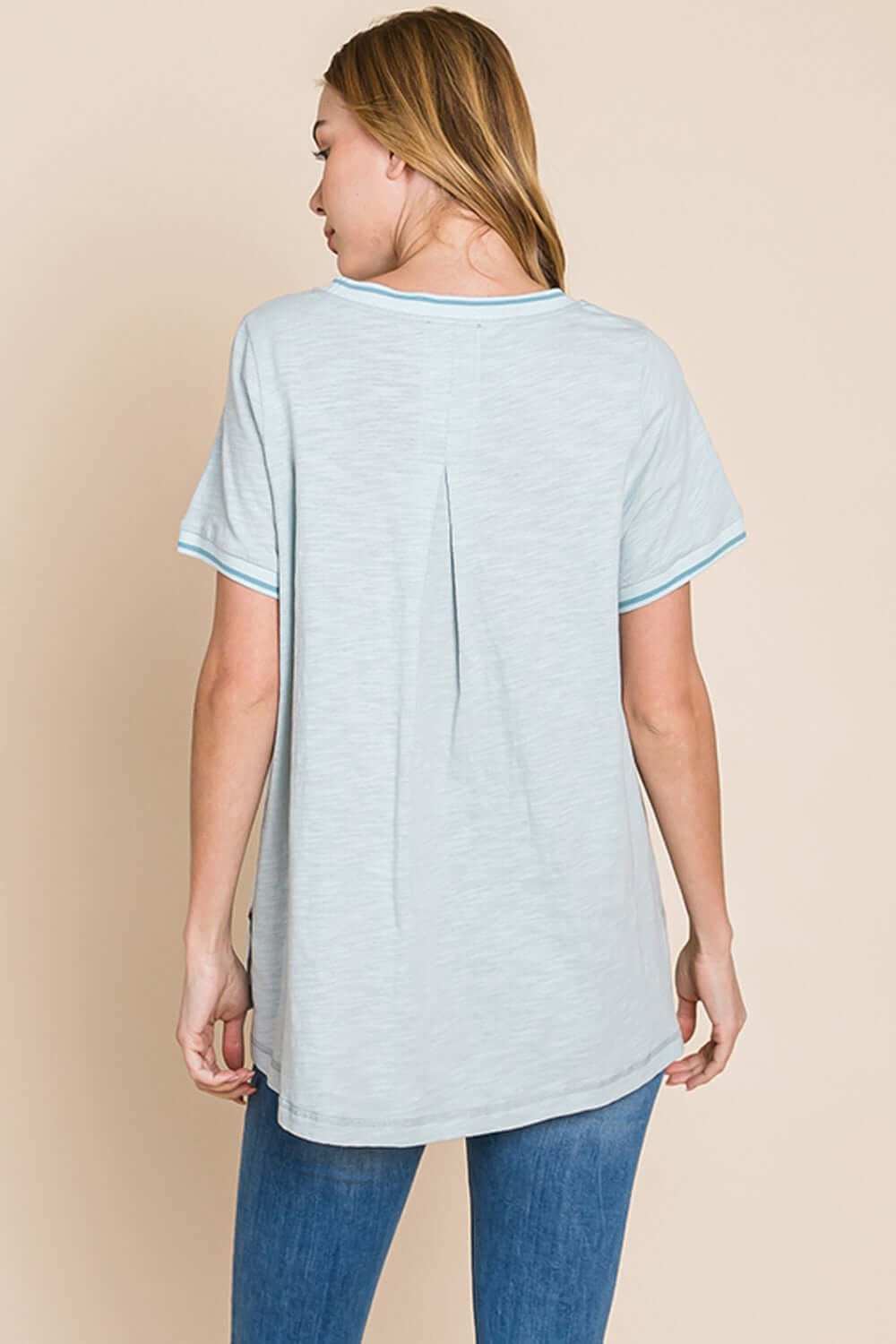 Woman wearing a contrast trim short sleeve slit T-shirt with jeans, showcasing the back view of the unique trim detail and side slit.