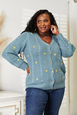 Woman wearing HEYSON floral embroidered cable cardigan, showcasing cozy and elegant knit fashion with button-down design.