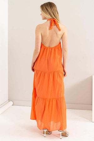 Back view of a woman in an orange halter neck maxi dress with tiered layers, perfect for warm days and tropical getaways.