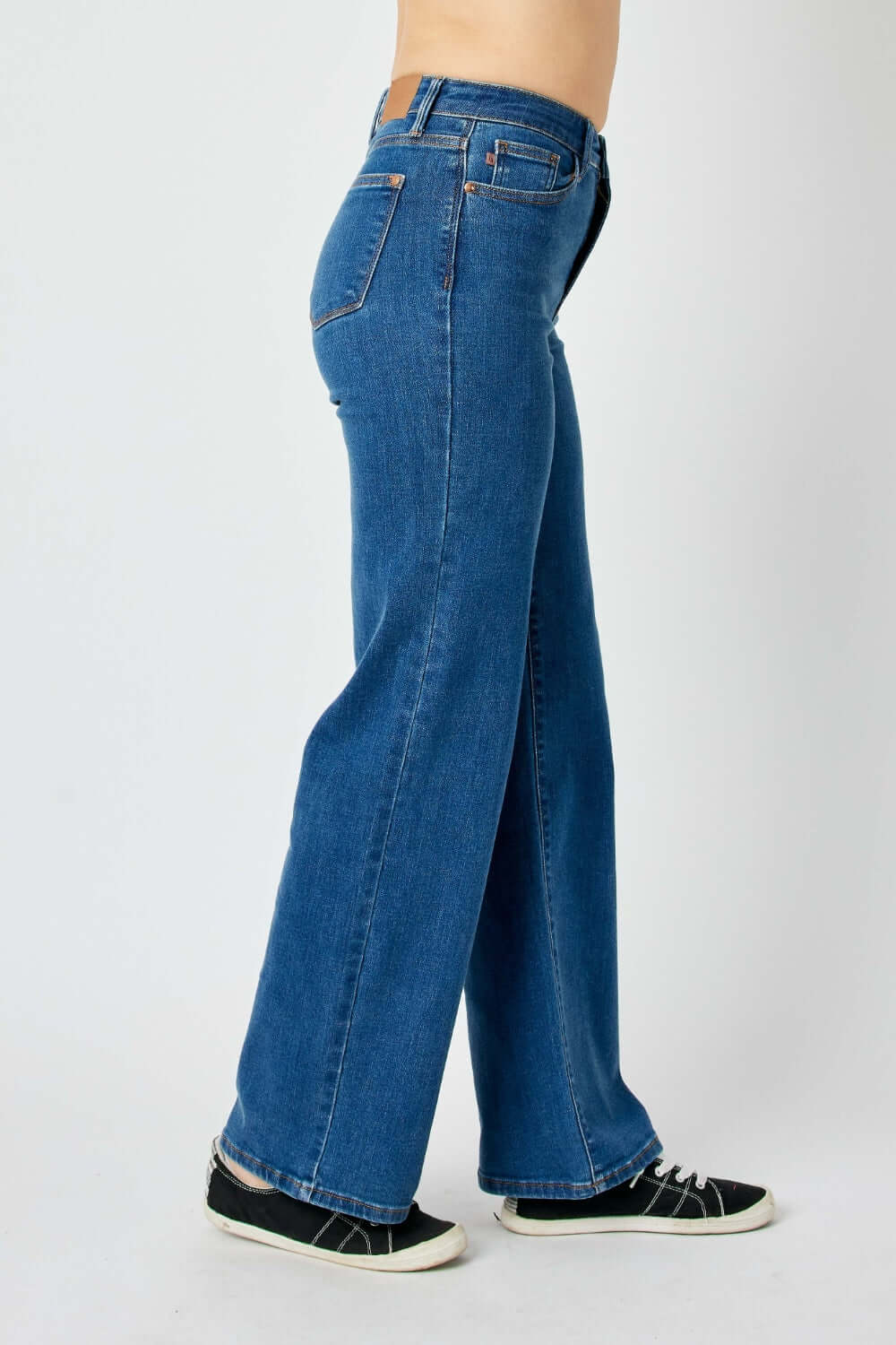 Side view of model wearing high-rise straight Judy Blue jeans in blue paired with casual shoes.