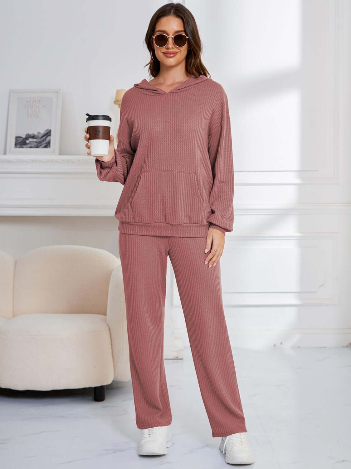 Woman in dusty pink Bella Road hoodie and pants set holding coffee, showcasing relaxed fit and cozy style.