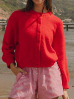 Model in a cozy red Bella Road Button Down Cardigan paired with striped shorts on a sunny beach day.