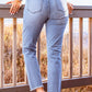 Stylish distressed cropped jeans in light blue, featuring back pockets and frayed hems, worn by a model standing on a wooden deck railing.