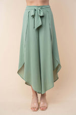 High-waisted green woven pants with a wide tulip hem and a tie at the waist for a stylish and comfortable fit.