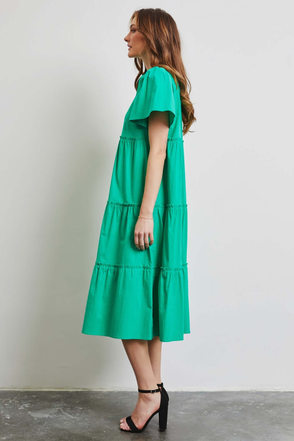 Woman wearing green HEYSON Cotton Poplin Ruffled Tiered Midi Dress, side view, showcasing elegant ruffles and a flattering silhouette.