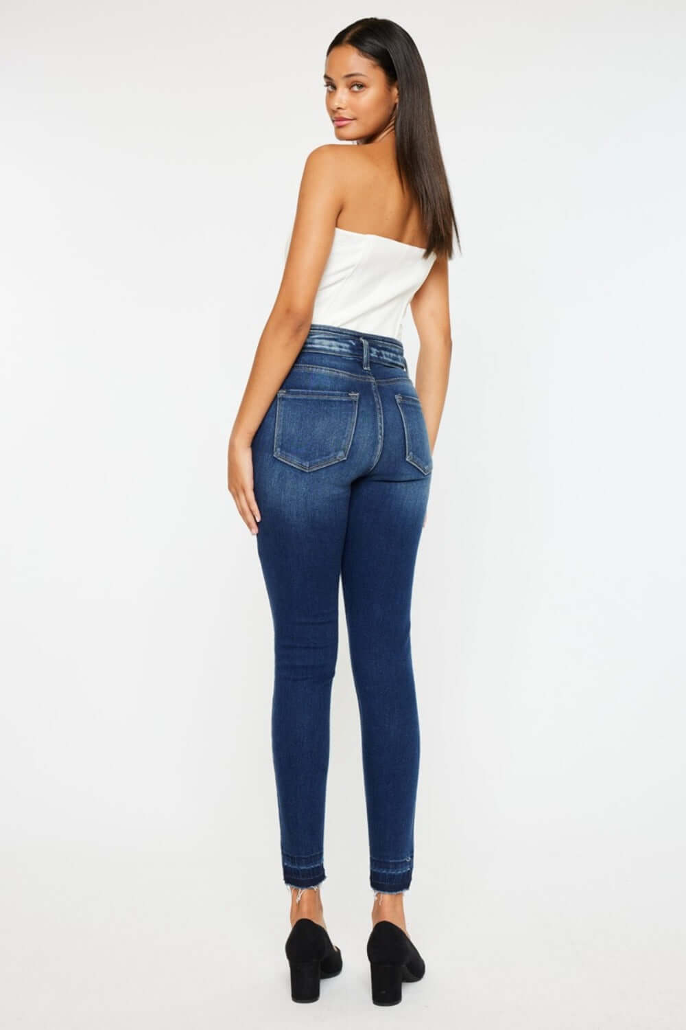 Woman wearing Kancan high-rise ankle skinny jeans with double waistband and release hem, showcasing trendy dark wash denim style.