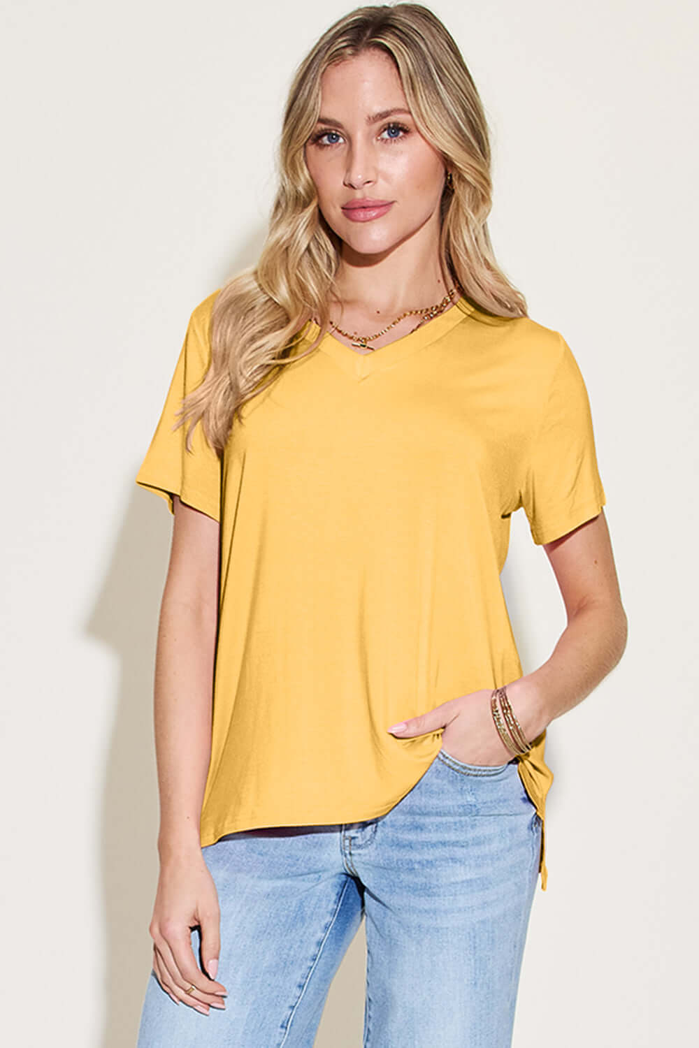 Woman wearing a yellow Bamboo V-Neck High-Low T-Shirt with blue jeans, showcasing the slightly stretchy material and basic style.