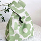 Eco-friendly green and white flower knitted handbag on a table with a plant in the background