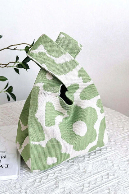 Eco-friendly green and white flower knitted handbag on a table with a plant in the background