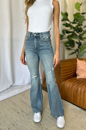 Woman wearing Judy Blue medium rise tummy control destroy flare jeans with distressed detailing, standing in a stylish room.