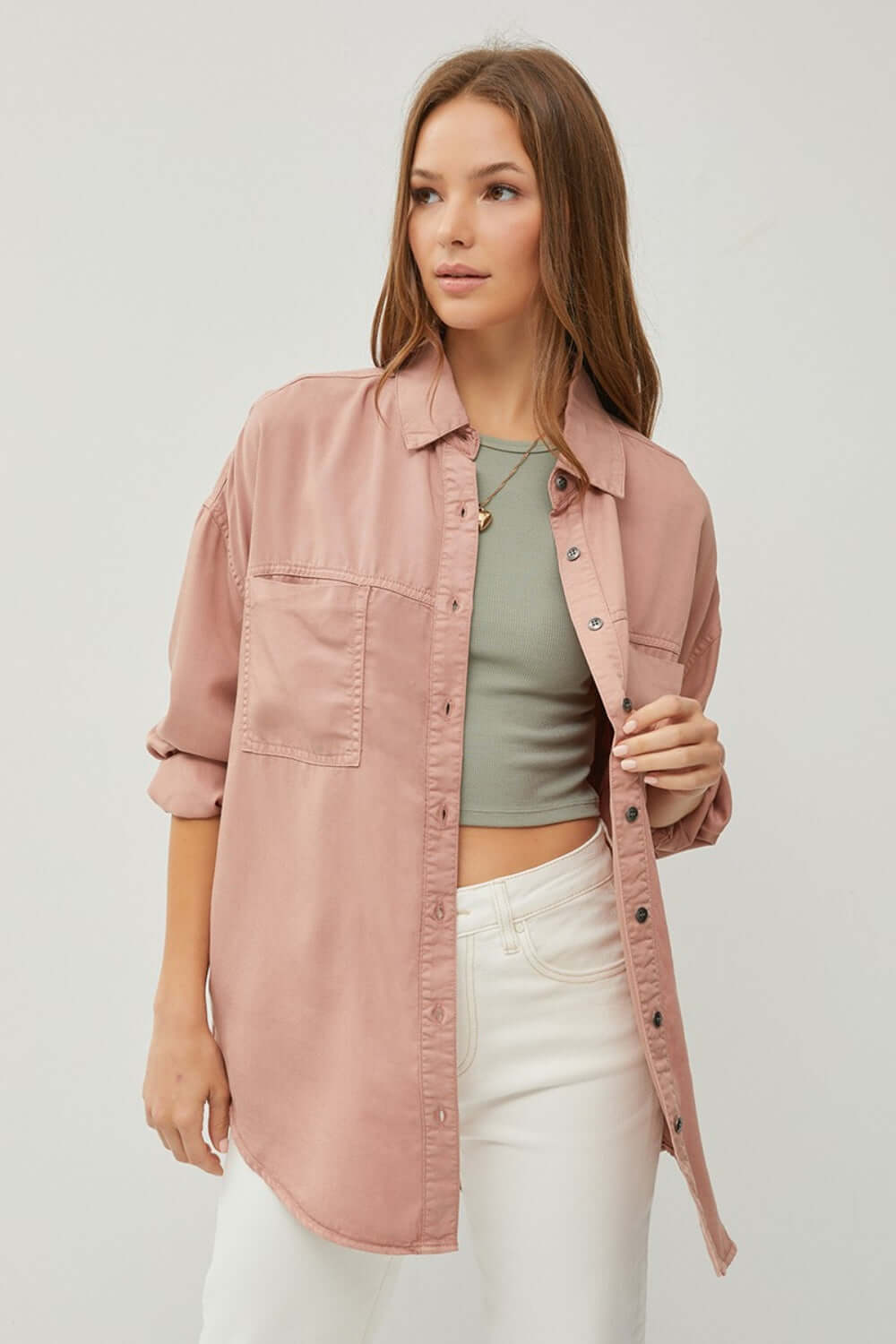 Woman wearing RISEN full size button-up long sleeve denim shirt in pink, styled with a crop top and white jeans