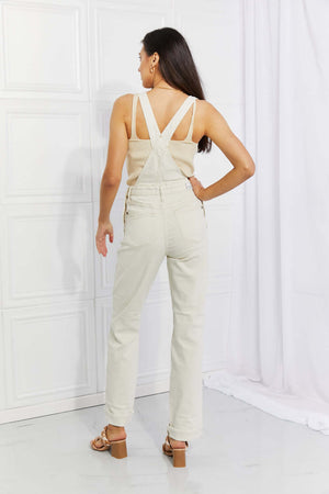 Woman wearing Taylor High Waist Overalls with beige tank top, showing back view. Full size Judy Blue Jeans, solid casual style with pockets.