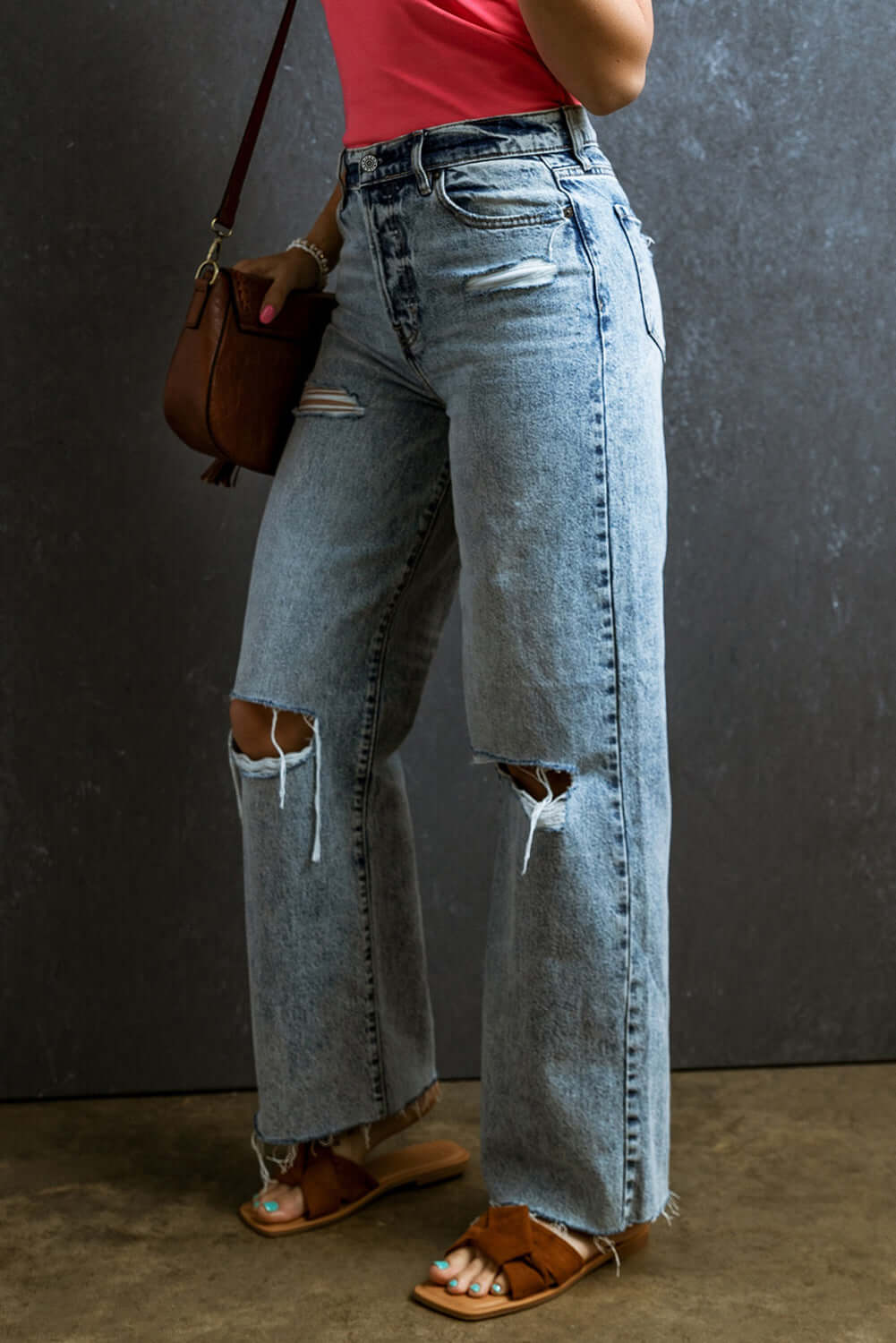 Petite distressed raw hem straight jeans with no stretch, featuring a trendy and playful fit, paired with sandals and a red top.