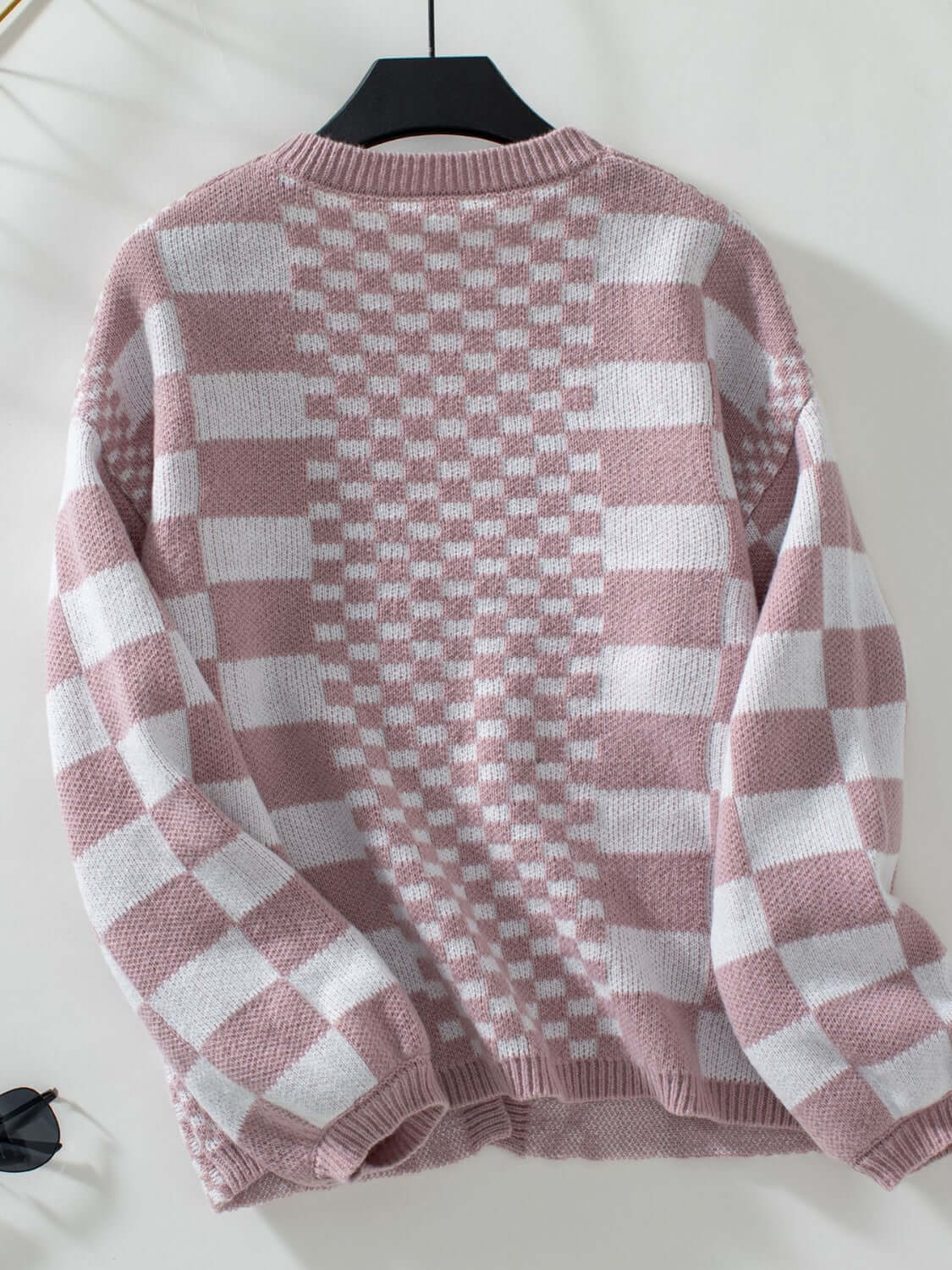 Dusty pink checkered open front cardigan with dropped shoulders, displayed on a hanger. Stylish and playful knitwear.