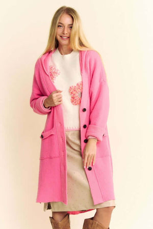 Stylish woman in a pink side slit hooded cardigan paired with a heart-patterned sweater and a chic skirt.